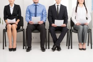 Four job applicants holding their CVs while sitting in a line