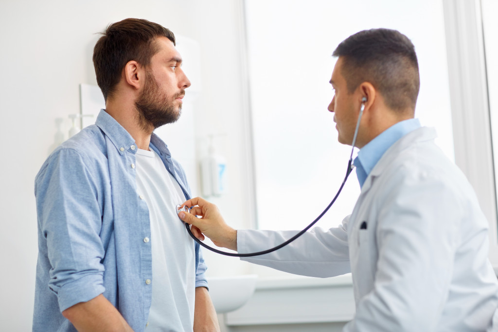 Male doctor checking the heart beat of a patient using a stethoscope in a hospital.