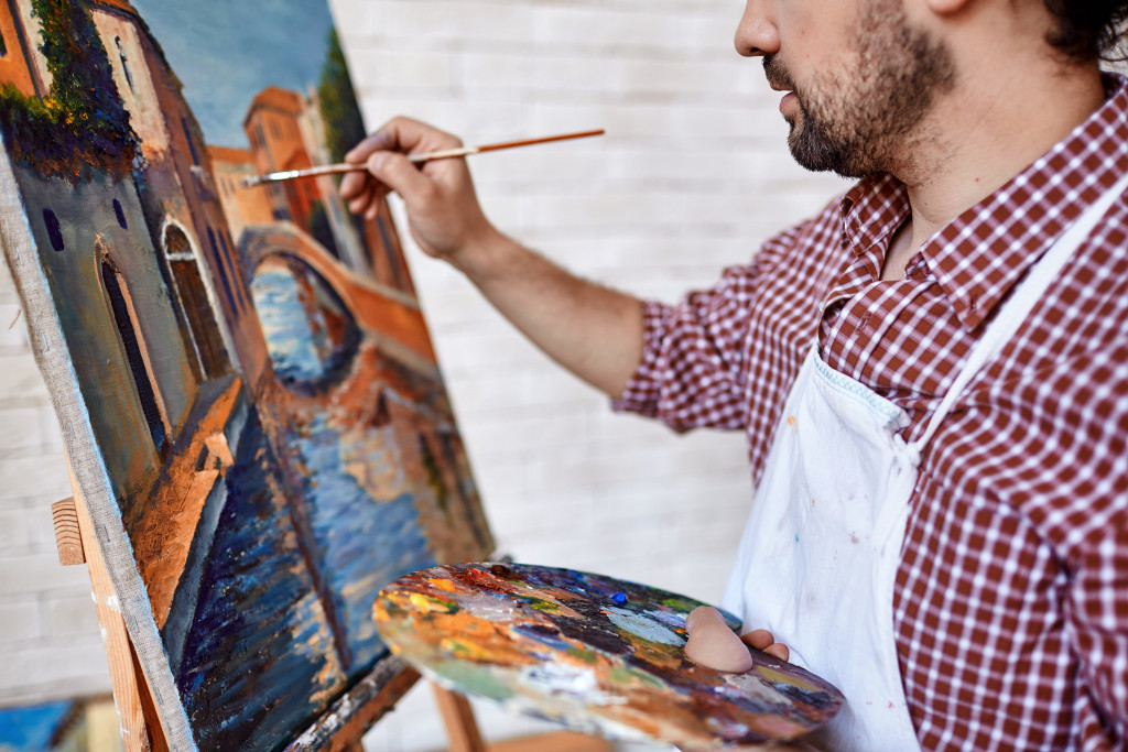 male artist painting landscape with oil paint on a canvas