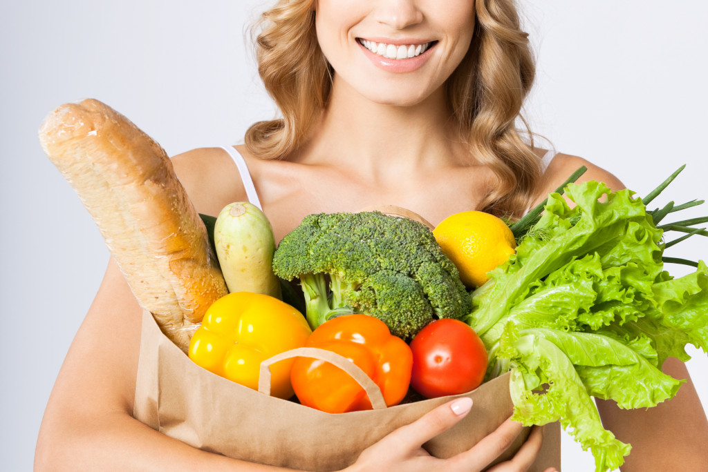 woman smiling while holding paper bag with fresh vegetables